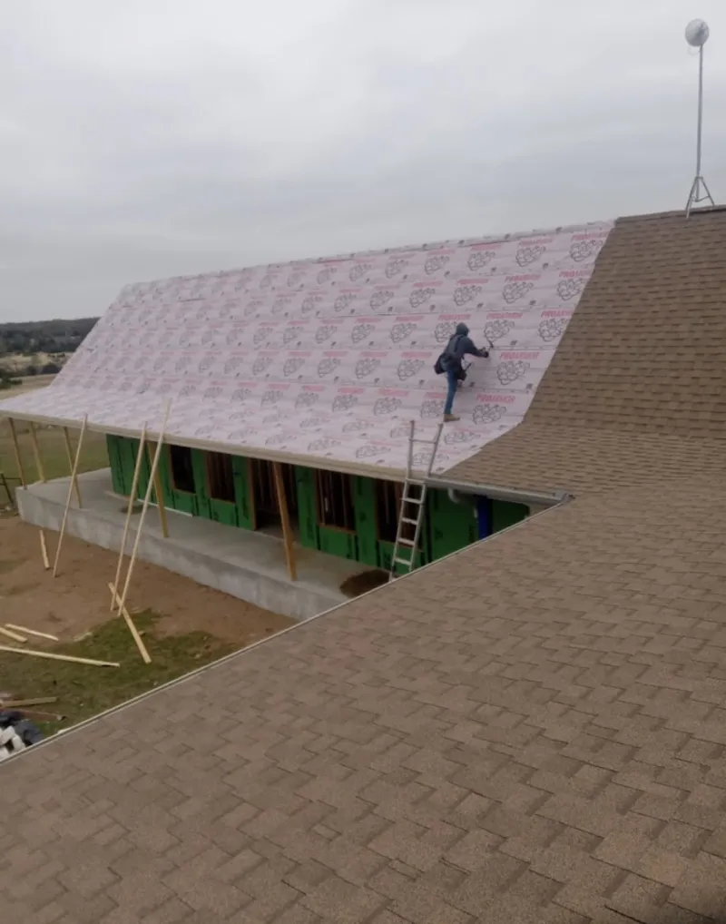 Worker preparing underlayment for a metal roof installation in Marilla